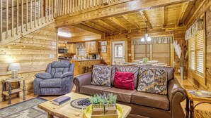 L’intérieur d’un chalet en bois, avec un canapé, un fauteuil, une table à manger et un coin cuisine.