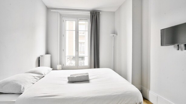 A minimalist bedroom with a large bed, a flat-screen TV, and a window with curtains. - Charmant T2 à 5 Minute de Paris (Issy-les-Moulineaux)