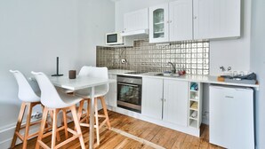 A compact kitchen with white cabinets, a microwave, a sink, and a dishwasher. There are two white chairs and a wooden stool. - Charmant T2 à 5 Minute de Paris (Issy-les-Moulineaux)