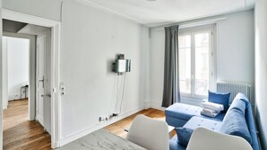 A modern, well-lit living room with a sofa, a small table, and a TV mounted on the wall. - Charmant T2 à 5 Minute de Paris (Issy-les-Moulineaux)