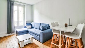 A modern living room with a sectional sofa, a dining table with chairs, a white coffee table, and a window with curtains. - Charmant T2 à 5 Minute de Paris (Issy-les-Moulineaux)
