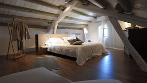 Ett sovrum med ett träpanelat tak, en säng med vita sängkläder, ett sängbord och en lampa.