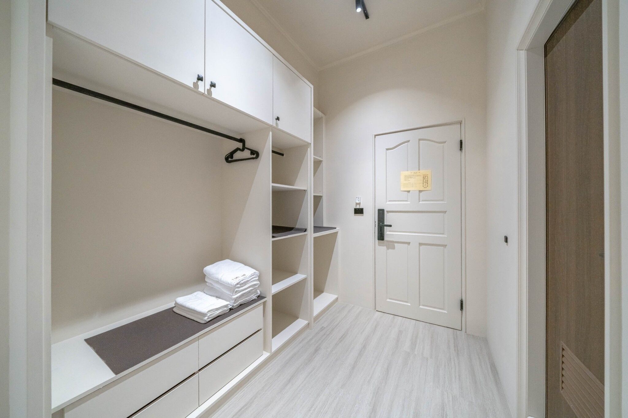 A hallway with a white wardrobe, a door with a sign, and a bench with folded towels.