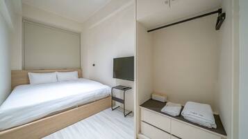 A modern hotel room with a bed, a TV, a small table, and a wardrobe.
