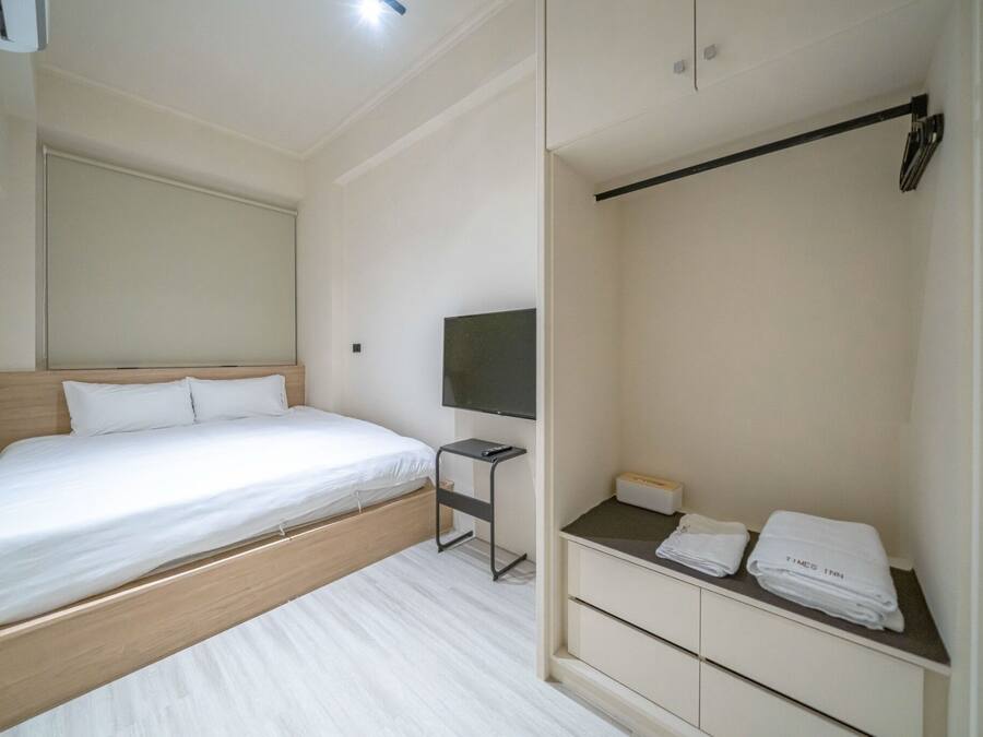 A modern hotel room with a bed, a TV, a small table, and a wardrobe.