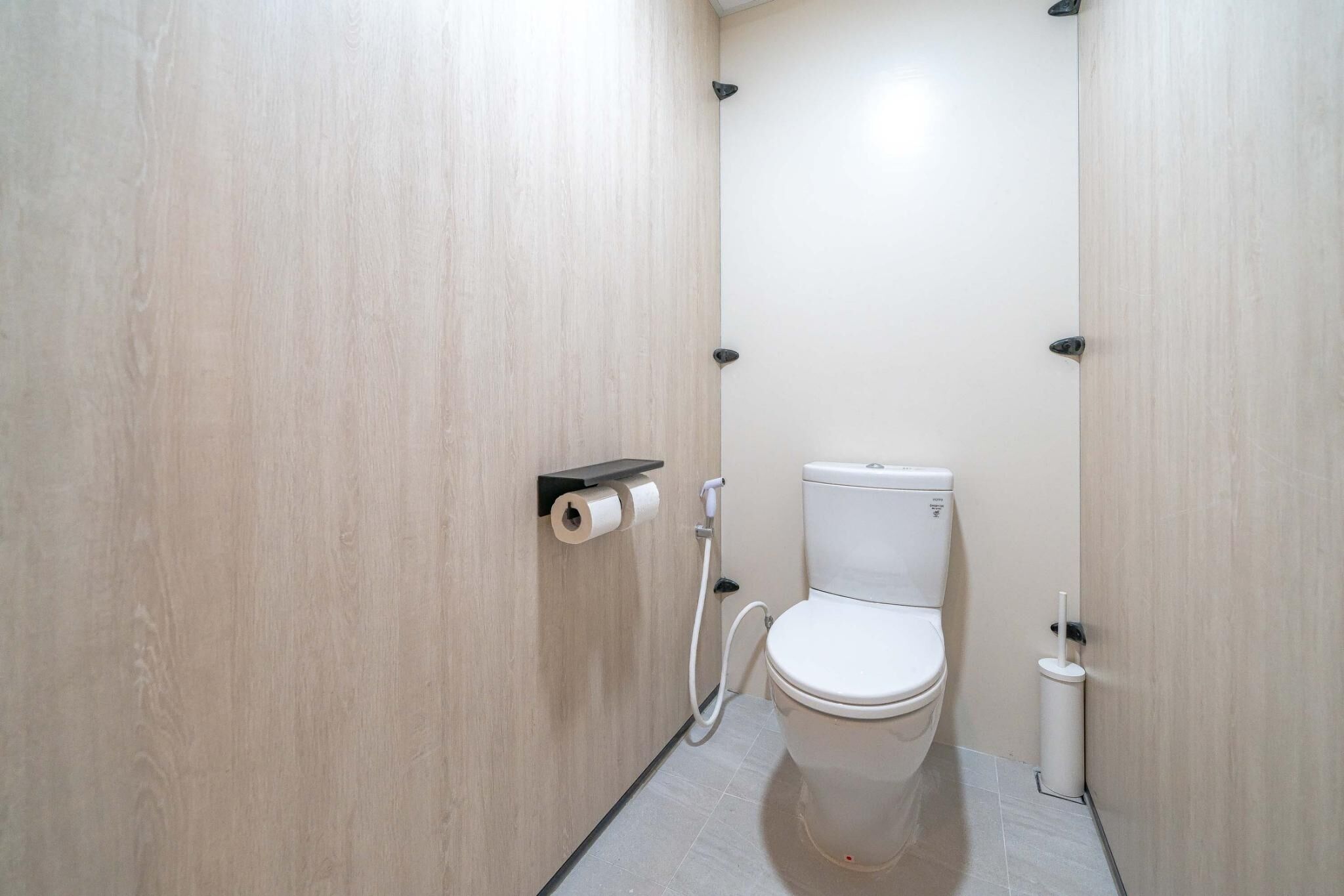 A small, modern bathroom with a toilet, a paper towel dispenser, and a toilet paper roll.
