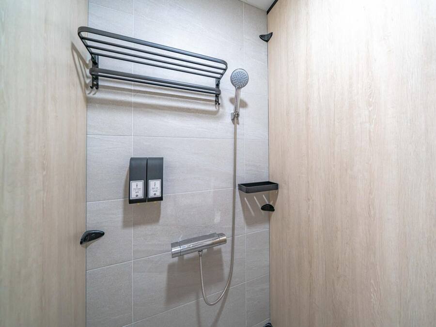 Una ducha moderna con cabezal de ducha de mano, un perchero y un dispensador de jabón.