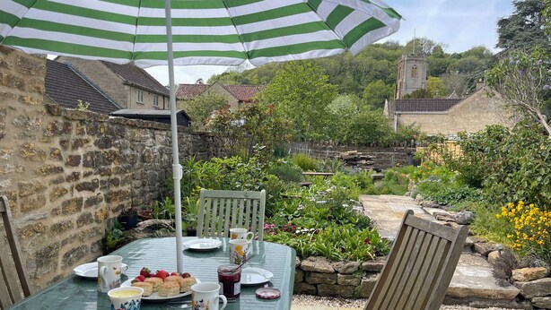A patio with a table set for tea, surrounded by stone walls and greenery.