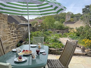 A patio with a table set for tea, surrounded by stone walls and greenery. - Two Towers Cottage (Montacute)