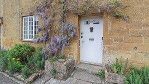 A stone building with a white door, number 23, and a small garden with purple flowers.