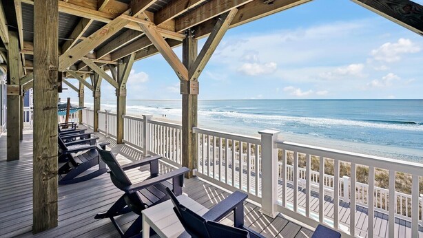 A wooden deck with seating overlooking a beach. - Admirals Lodge | Pool & Hot tub | Games | Oceanfront (Oak Island)