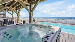 A wooden deck with a hot tub and pool overlooking a beach. - Admirals Lodge | Pool & Hot tub | Games | Oceanfront (Oak Island)