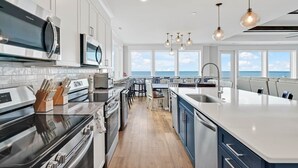 A modern kitchen with a large island, stainless steel appliances, and a view of the ocean. - Admirals Lodge | Pool & Hot tub | Games | Oceanfront (Oak Island)