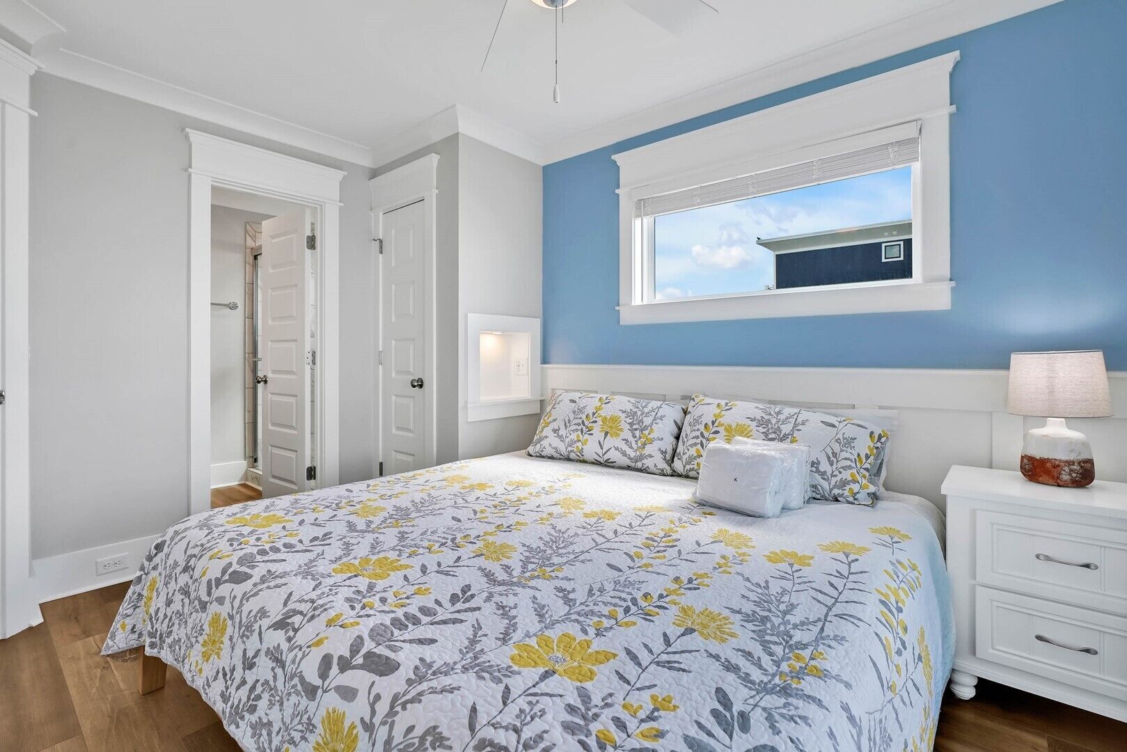 Une chambre à coucher avec un grand lit, une table de chevet, une fenêtre avec des stores et une porte donnant sur une autre pièce.