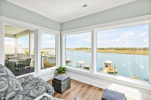 Una stanza spaziosa con ampie finestre vista su un corpo d'acqua, un balcone con mobili da esterno e una zona relax accogliente.