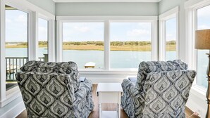 Quarto com duas poltronas estampadas voltadas para uma janela ampla com vista para um corpo d'água e uma paisagem gramada.