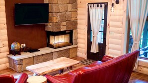 Een gezellig houten blokhut interieur met een stenen open haard, leren bank en een flatscreen televisie aan de muur.
