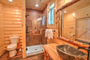 Features a compact bathroom with a toilet, glass-enclosed shower, and wooden vanity with a large sink.