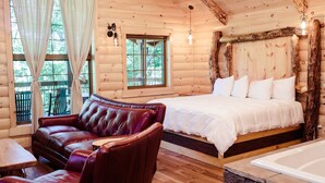 Een slaapkamer in een blokhut met een groot bed, een leren bank, een houten vloer en een ligbad van steen.