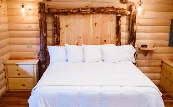 A wooden log cabin bedroom with a bed, bedside tables, and a rustic headboard.