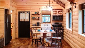 Een houten houten hut interieur met een keuken voorzien van een koelkast, fornuis, magnetron en spoelbak. Er is een eettafel met stoelen en een hanglamp.