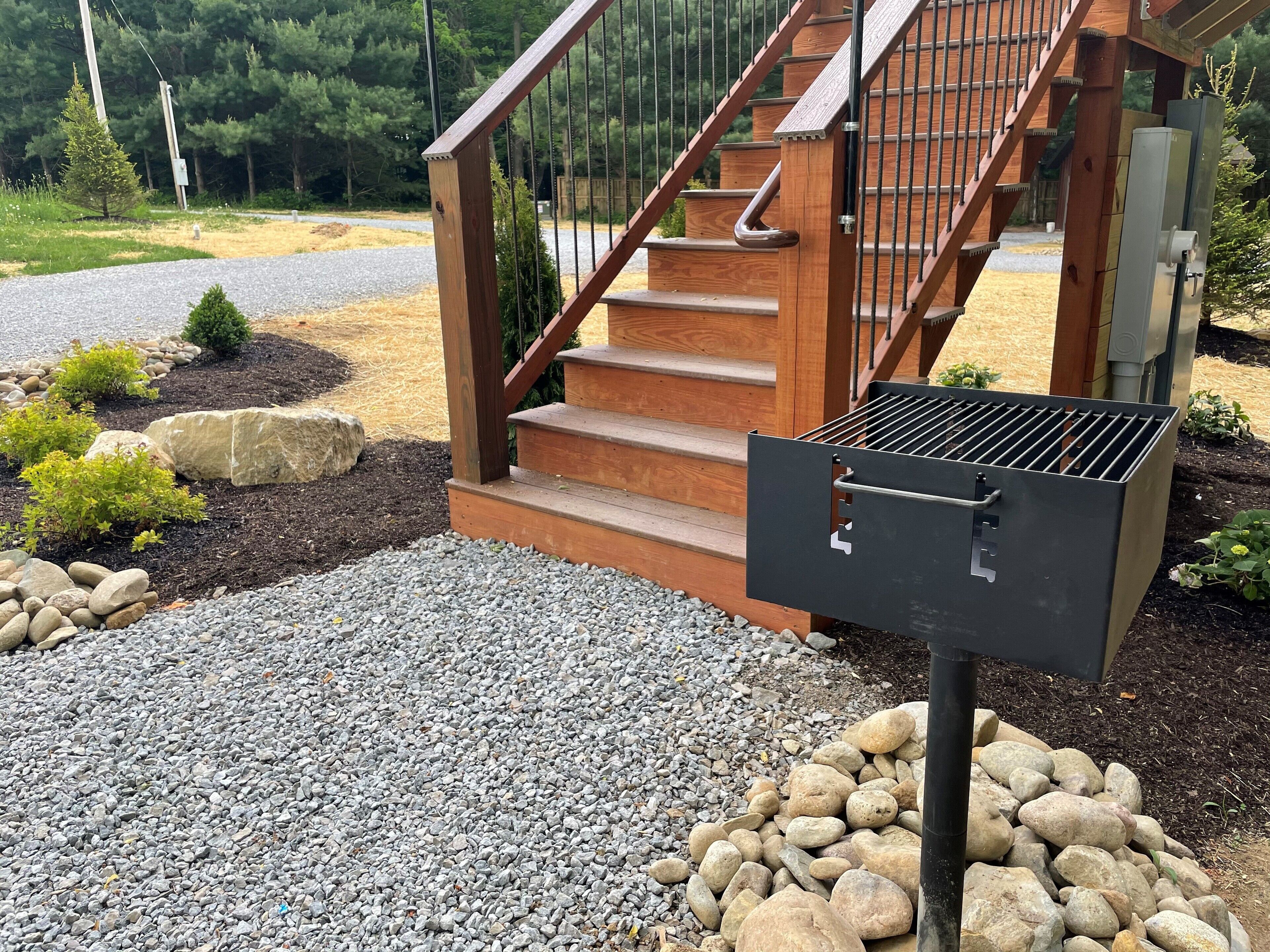 A wooden staircase with a metal grill attached to a post, surrounded by gravel and rocks.