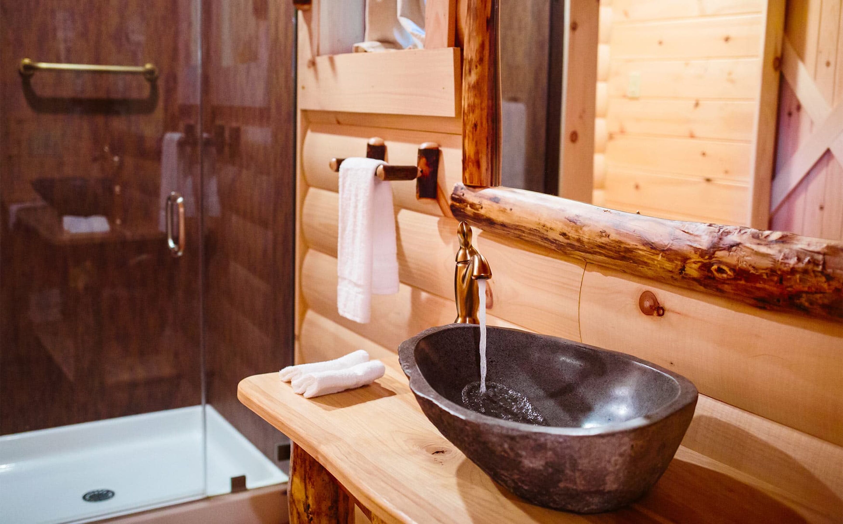 Une salle de bain rustique avec un lavabo en bois, une cabine de douche en verre et un mur en bois.