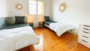 Habitación con dos camas individuales, piso de madera, un radiador y dos lámparas fijadas a la pared.