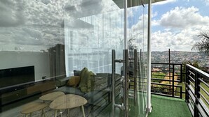 A modern living room with a large TV, comfortable seating, and a balcony with a view. - Prayer mountain Cove -tranquility and cosiness at its best. Incredible views! (Kampala)