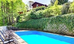 A swimming pool with lounge chairs, surrounded by greenery and a stone wall.
