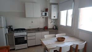 A compact kitchen with a gas stove, oven, and microwave, a small sink, and a dining area with a table and chairs.