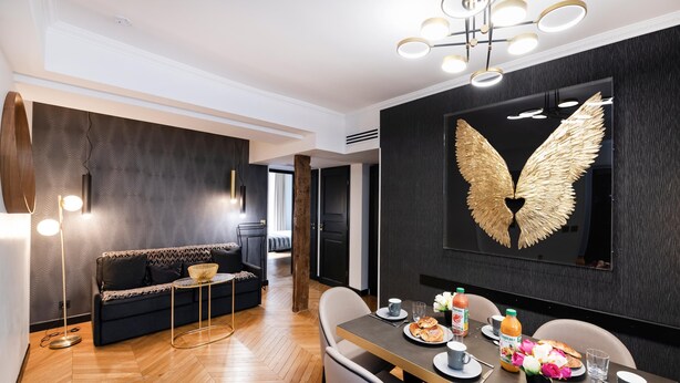 Un comedor moderno con piso de madera en espiga, un sofá de color oscuro y una mesa de comedor dispuesta con platos, vasos y un centro de mesa decorativo.