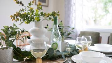 Une table à manger ornée d’un vase blanc, d’une bouteille et de deux verres de vin blanc, le tout entouré de plantes vertes.
