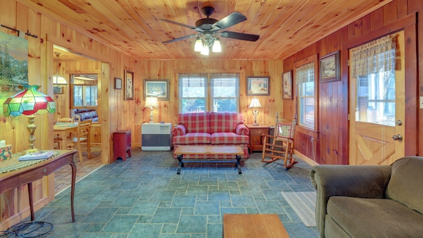 A wooden cabin interior with a plaid sofa, a brown couch, a dining table, and a ceiling fan. - Dog-friendly Burnsville Home w/ Patio & Trails! (Burnsville)