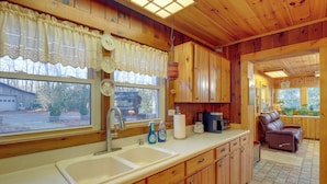 A wooden cabin kitchen with a large window, a sink, cabinets, and a leather couch in the dining area. - Dog-friendly Burnsville Home w/ Patio & Trails! (Burnsville)