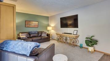 A living room with a sofa, a small round table, a TV mounted on the wall, a decorative console table, and a potted plant.