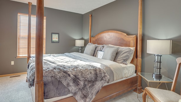 A four-poster bed with a wooden headboard, two bedside lamps, and a chair. - Akron Home w/ Deck: Walk to Towpath Trail! (Akron)