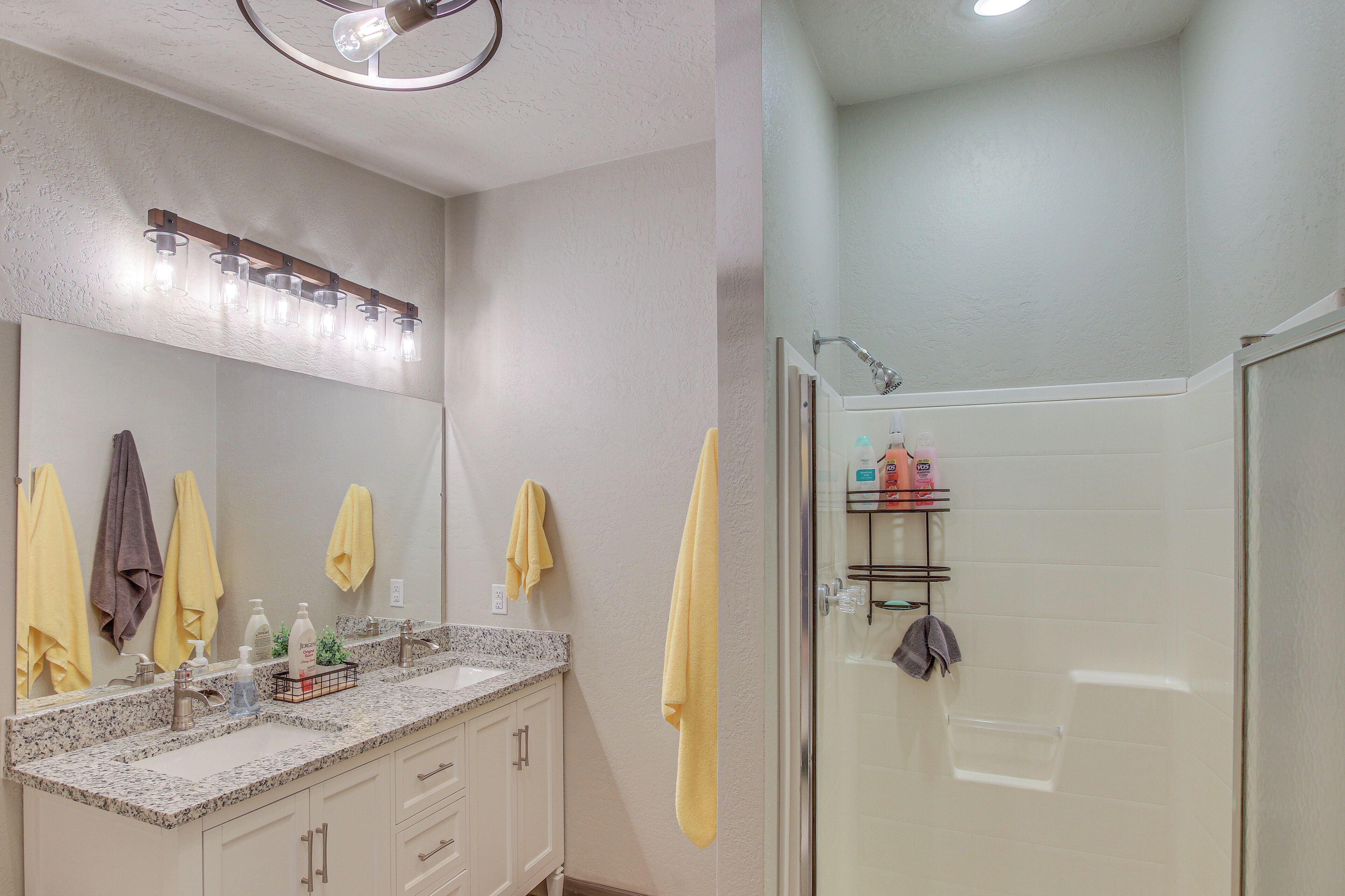 A bathroom with a granite countertop, a sink, a mirror, and a shower area.