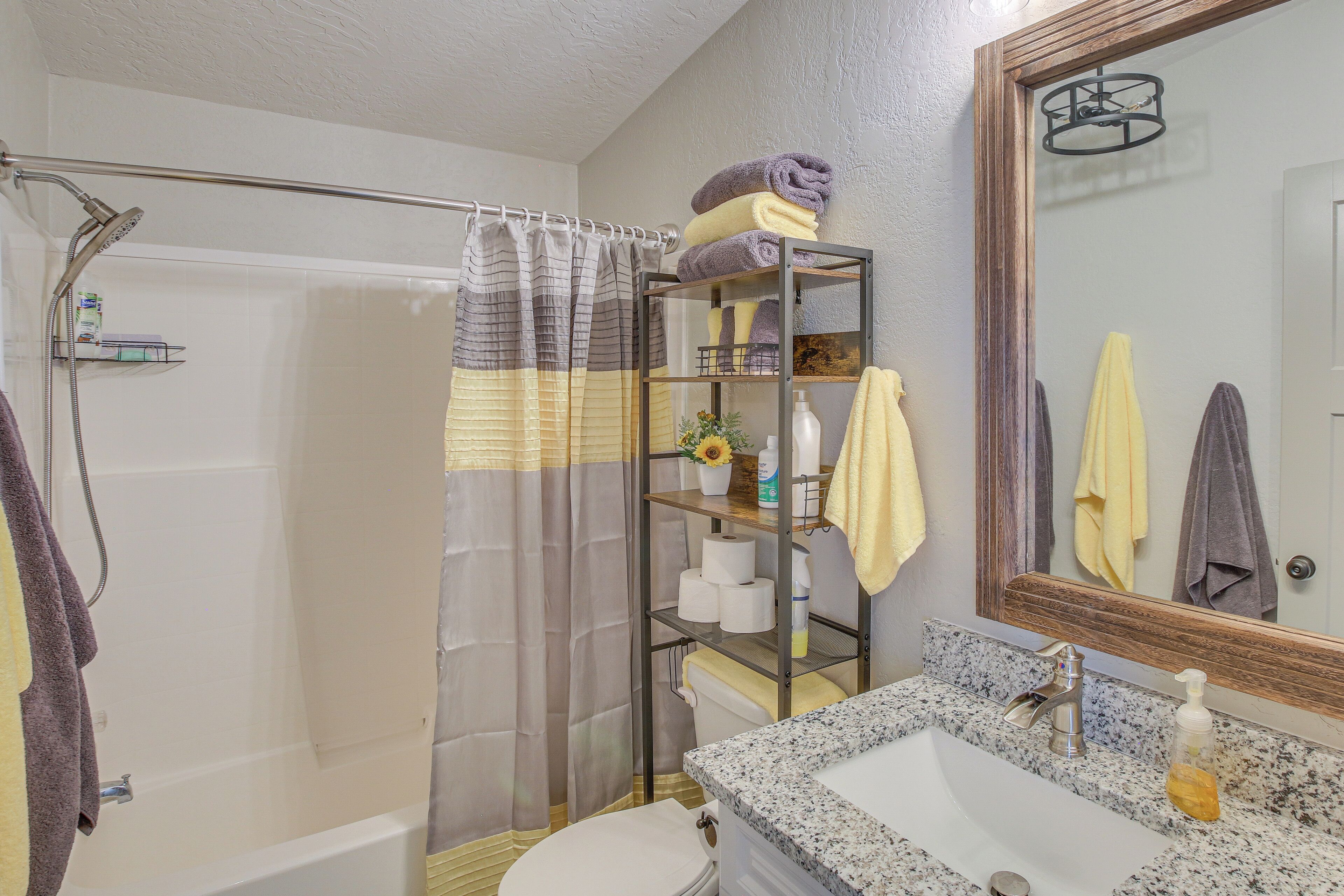 A bathroom with a shower, toilet, sink, and a shelf with towels and toiletries.