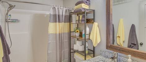 A bathroom with a shower, toilet, sink, and a shelf with towels and toiletries.