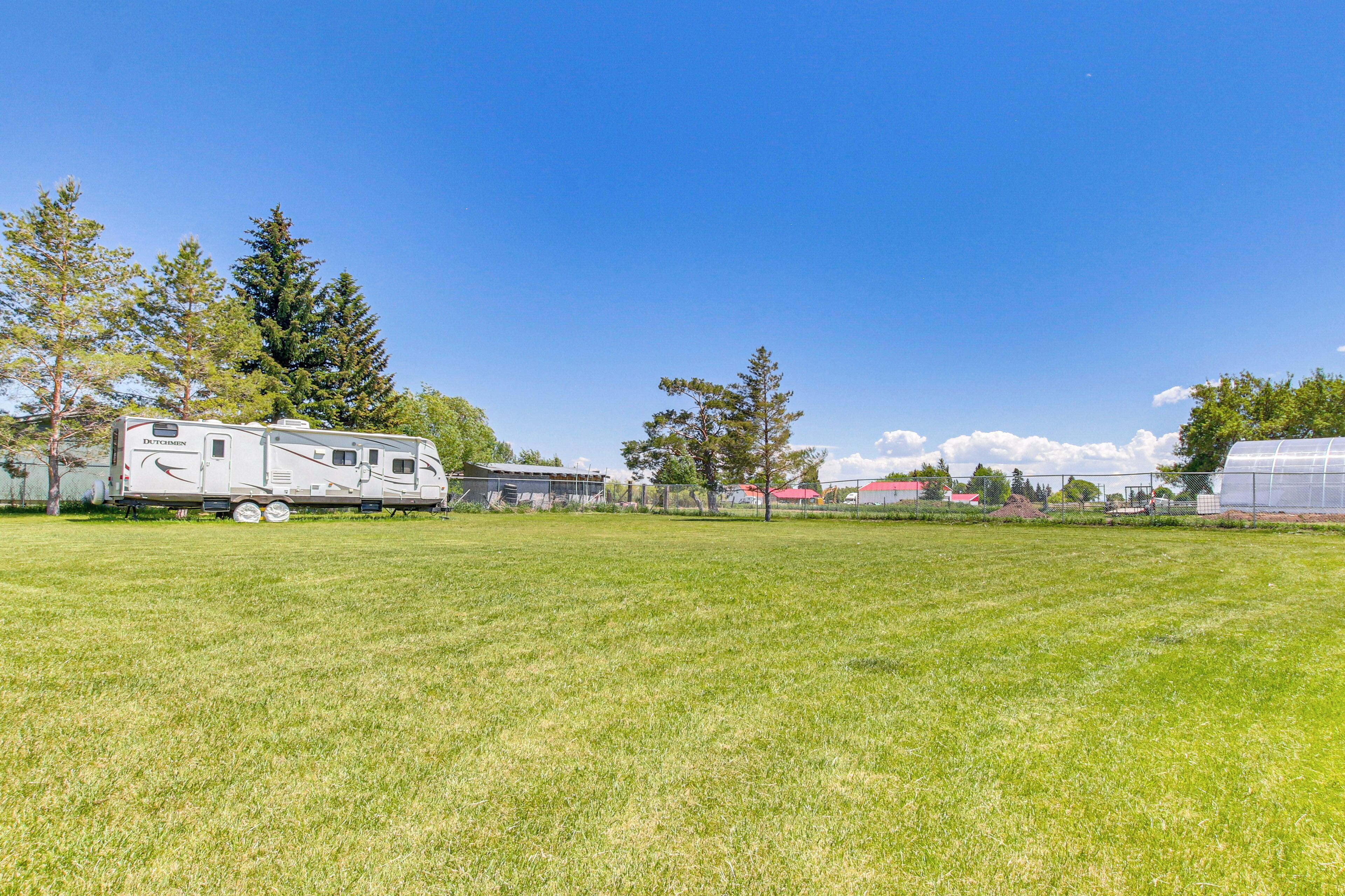 A grassy field with a white RV and a greenhouse.