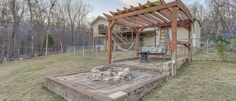 A covered outdoor seating area with a fire pit, a wooden pergola, and a staircase leading to a second level.