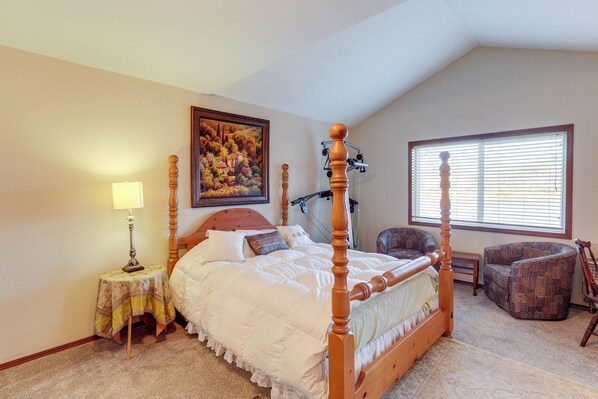 A bedroom with a four-poster bed, a chair, a lamp, a painting, and a window with blinds.
