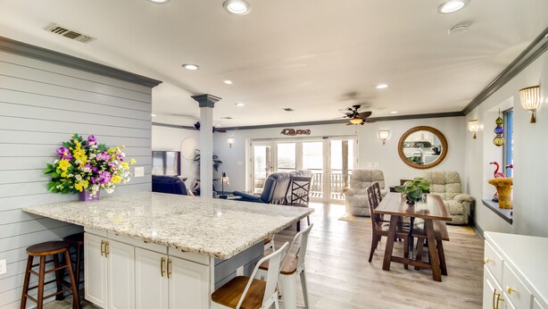 A modern kitchen with a central island, bar stools, and a dining area with a wooden table and chairs. - Front Row Beachfront Long Beach Getaway (Long Beach)