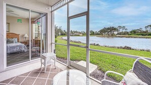 A room with a bed, a chair, and a view of a lake through large windows. - Naples Condo w/ Pond Views & Patio - Near Golf! (Naples)