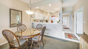 A dining area with a glass table, wooden chairs, a chandelier, and a kitchen in the background. - Naples Condo w/ Pond Views & Patio - Near Golf! (Naples)