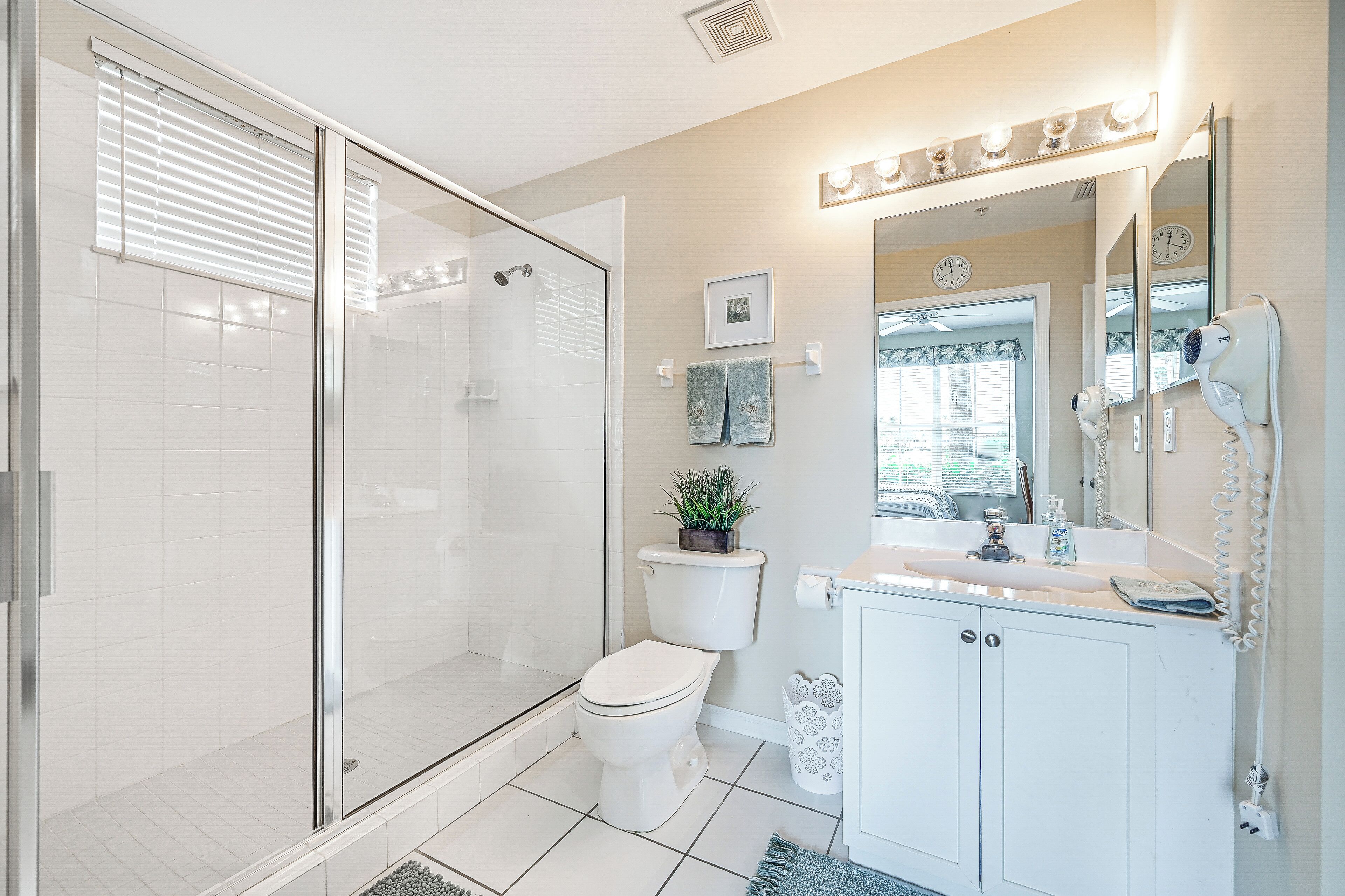 Une salle de bain moderne avec une douche à l’italienne en verre, des toilettes, un lavabo avec un meuble-vasque et un miroir avec des lumières au-dessus.