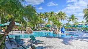 A pool area with lounge chairs, umbrellas, and palm trees. - Naples Condo w/ Pond Views & Patio - Near Golf! (Naples)