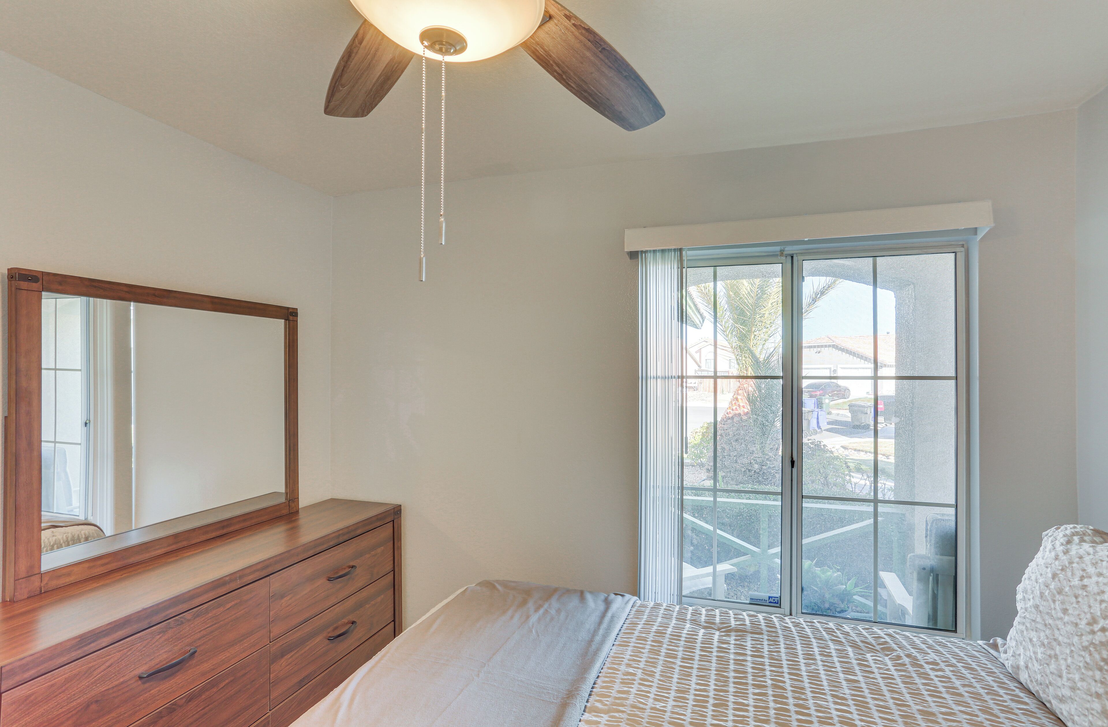 A bedroom with a bed, a dresser, a ceiling fan, and a window with a view of the outside.