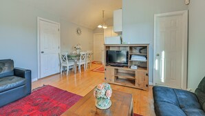 Una sala de estar con sofá, una mesa de centro con un florero, un televisor sobre un mueble de madera, y un comedor con sillas y una mesa.